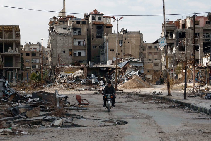 A man drives a motorbike past damaged buildings on Feb. 10 in Harasta, Syria. 