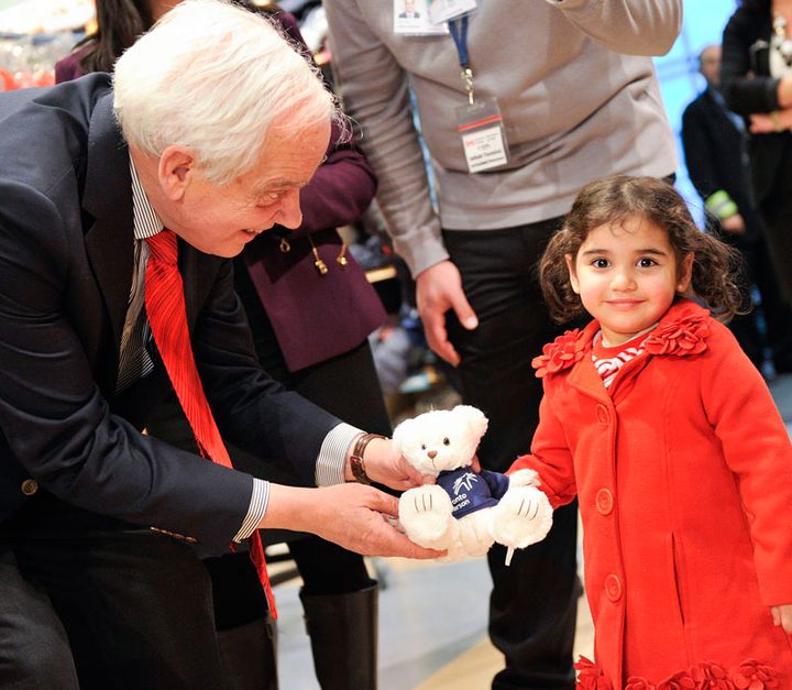 Canadian immigration minister John McCallum gives a teddy bear to a young Syrian girl.