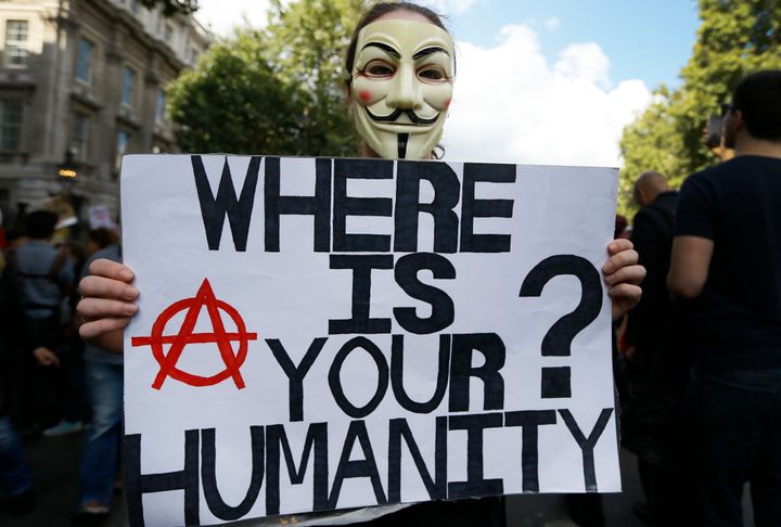 A masked demonstrator holds a banner during a Solidarity with Refugees march from Marble Arch to Parliament in London