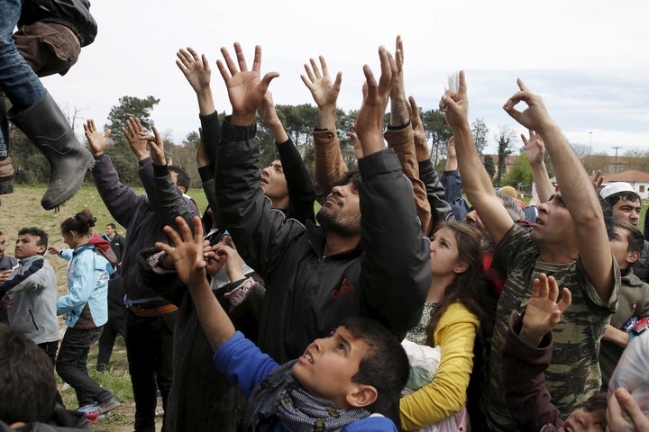 Migrants and refugees reach out to get humanitarian aid at a makeshift camp.