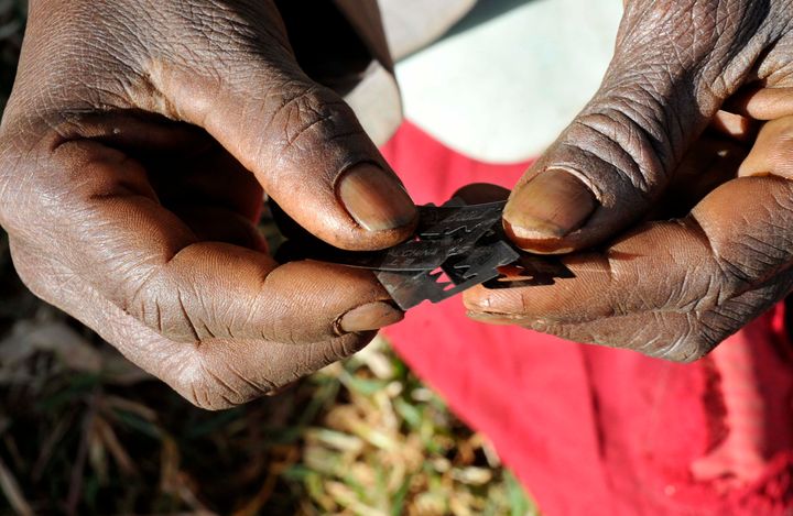 Prisca Korein, a traditional surgeon, holds razor blades before carrying out female genital mutilation on teenage girls from the Sebei tribe in Uganda.