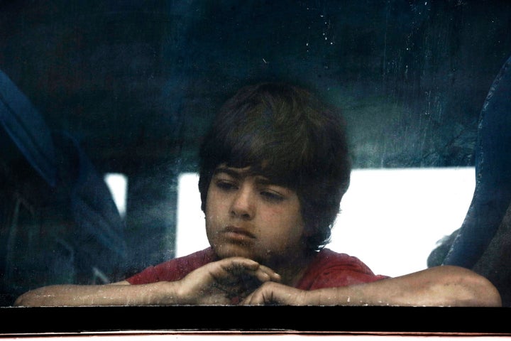 A boy sits on a bus as he waits to be transferred to a reception center.