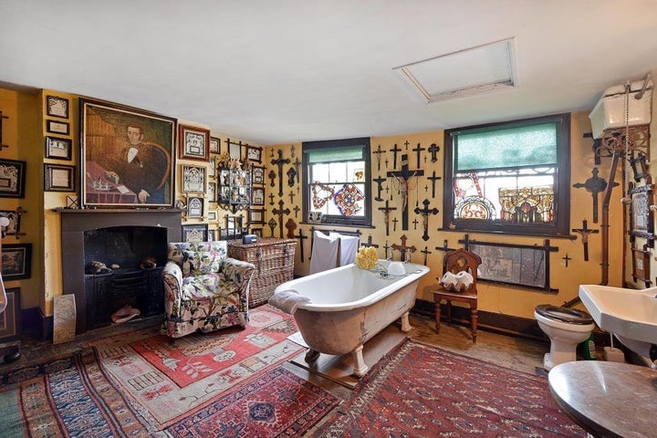 A wrought iron bathtub sits atop Persian rugs under a wall of crucifixes 