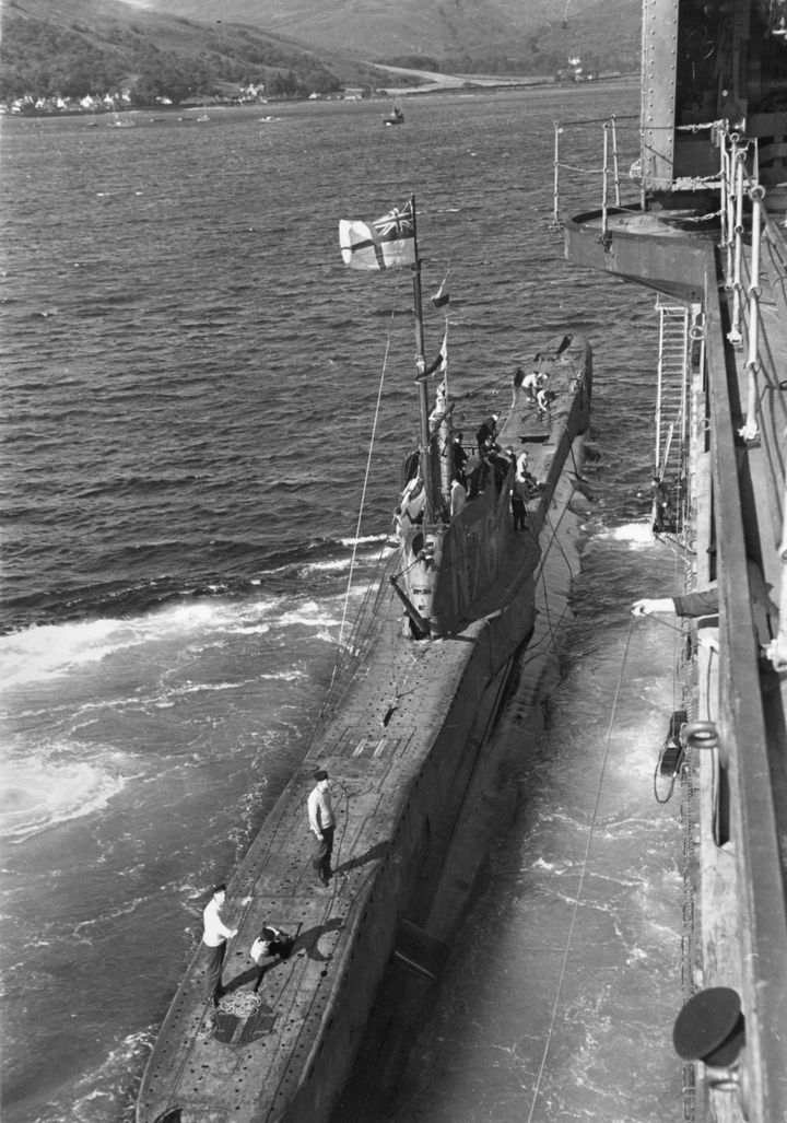 A British submarine returning from patrol docks next to a ship off the coast of British in 1940 