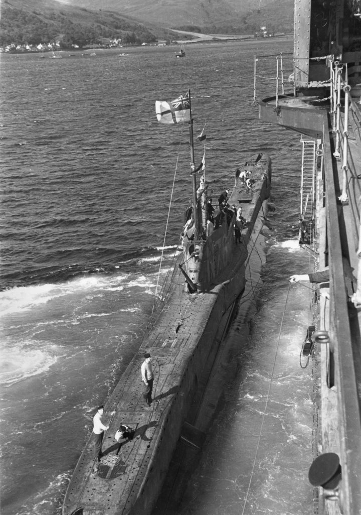A British submarine returning from patrol docks next to a ship off the coast of British in 1940