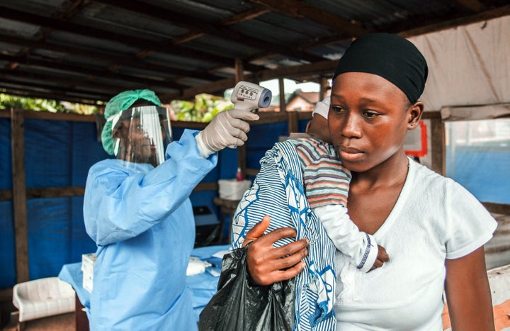 A woman visits the Macauley government hospital in Freetown, Sierra Leone, with her baby. She is having her temperature taken prior to entering, as part of Ebola prevention.