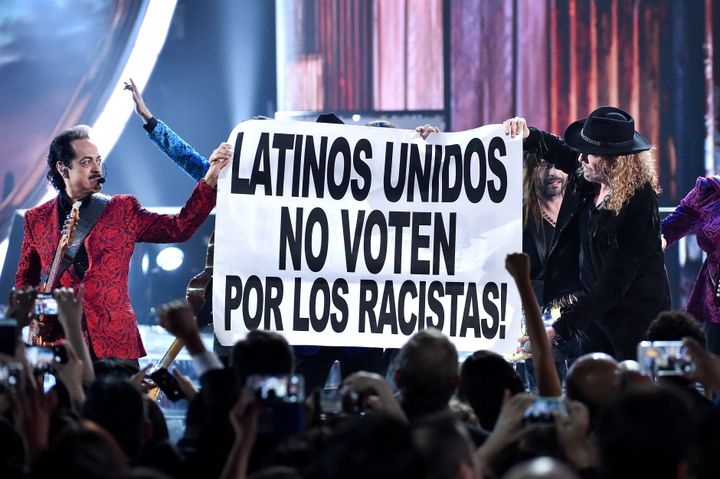 Mexican bands Maná and Los Tigres Del Norte hold up a sign that reads "Latinos United Don't Vote For Racists" onstage during the 16th annual Latin Grammy Awards.
