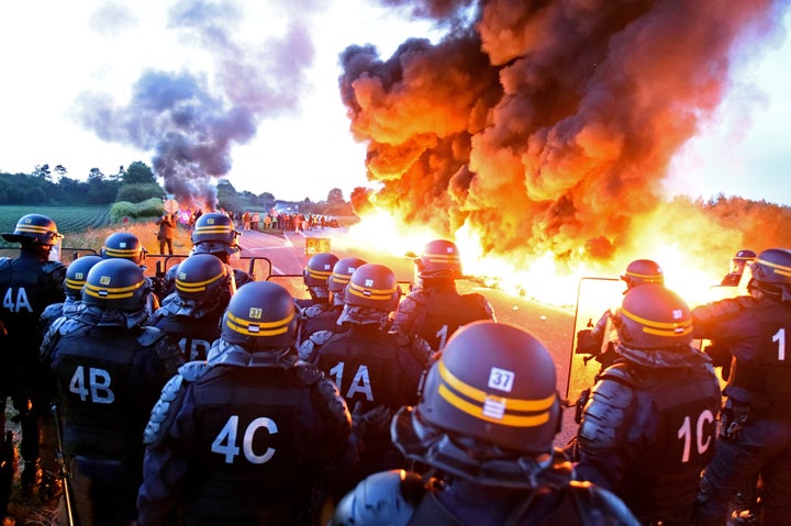 Riot police stand guard behind a fire as refinery workers hold a blockade of the oil depot of Douchy-Les-Mines