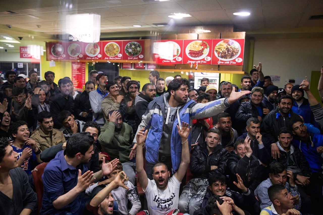 A group of refugees gather on April 2, 2016 to watch a Barcelona vs. Real Madrid soccer game inside the gas station cafe.