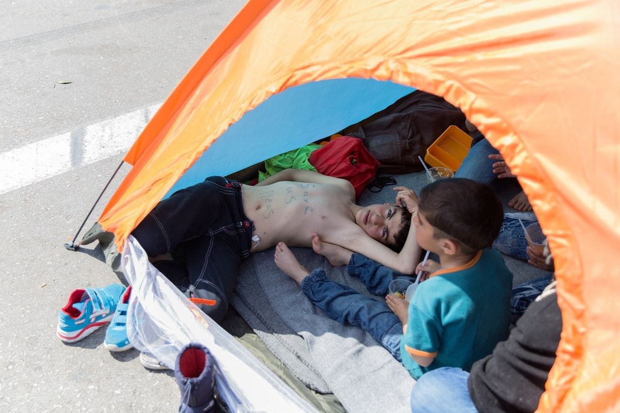 Hadi Al Ishkey, 10, from Damascus, lies in a tent pitched on the highway to protest the border closure between Greece and Macedonia, his chest reading, "Save us please." 