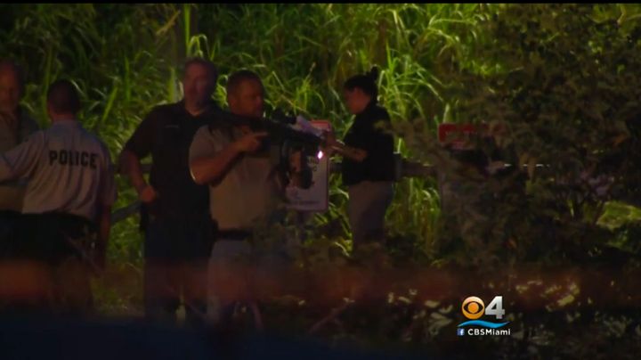 A Davie police officer is seen carrying a firearm as officers investigate a body found in a canal.
