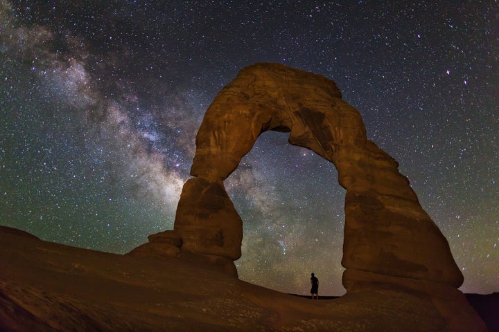 A person watches the Milky Way while standing inside Utah's Delicate Arch.