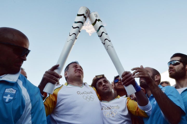 Hellenic Olympic Committee President Spyros Kapralos (2nd L) hands the Olympic Flame to Syrian refugee Ibrahim al-Hussein (C), 27, an amputee swimmer at the Eleonas refugee camp in Athens on April 26, 2016.