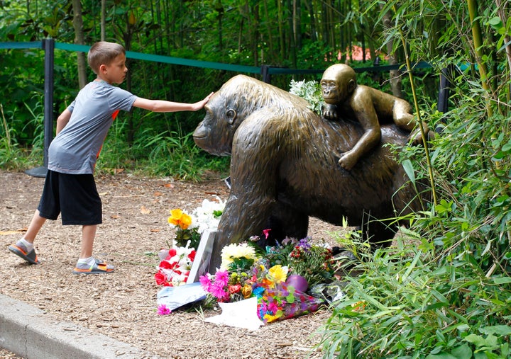 Visitors view a bronze statue of a gorilla and her baby surrounded by flowers outside the Cincinnati Zoo's Gorilla World exhi