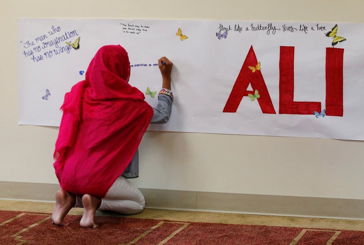 A member of the Louisville Islamic Center writes messages on a memorial banner as she pays her respect to Muhammad Ali, the f