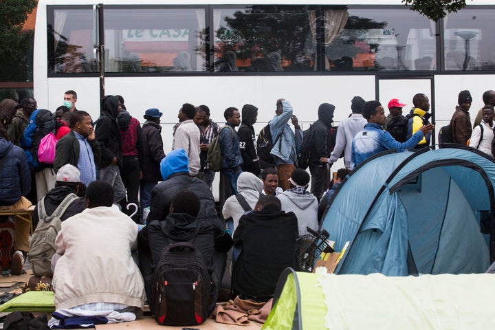 Migrants stand in line next to a bus during the evacuation of the migrants camp at Jardin d'Eole, in Paris on June 6, 2016.