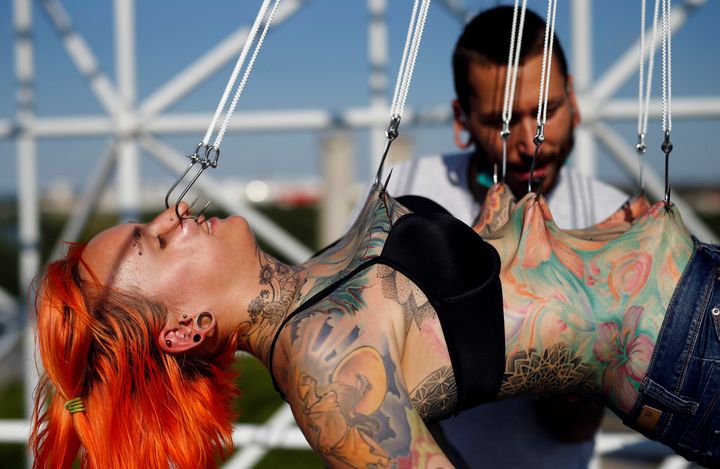 Professional body artist Dino Helvida (R), 27, inspects Kaitlin, 28, from the United States, as she is suspended from hooks pierced through her skin.