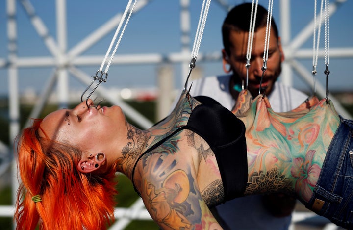 Professional body artist Dino Helvida (R), 27, inspects Kaitlin, 28, from the United States, as she is suspended from hooks p