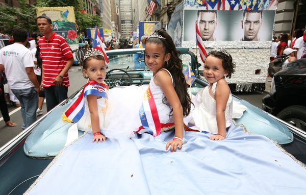 Three young girls ride in the back of a blue car along the parade route.&nbsp;