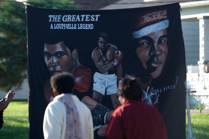 People walk in front of a banner in front of the boyhood home of Muhammad Ali on Grand Avenue before the passing of the funeral processional.