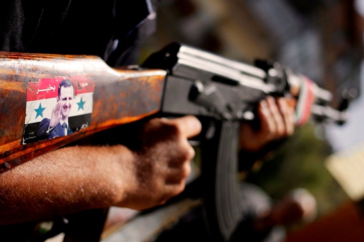 A Syrian soldier holds an AK-47 with a sticker of Syrian president Bashar al-Assad as he stands guard at a checkpoint in Dama
