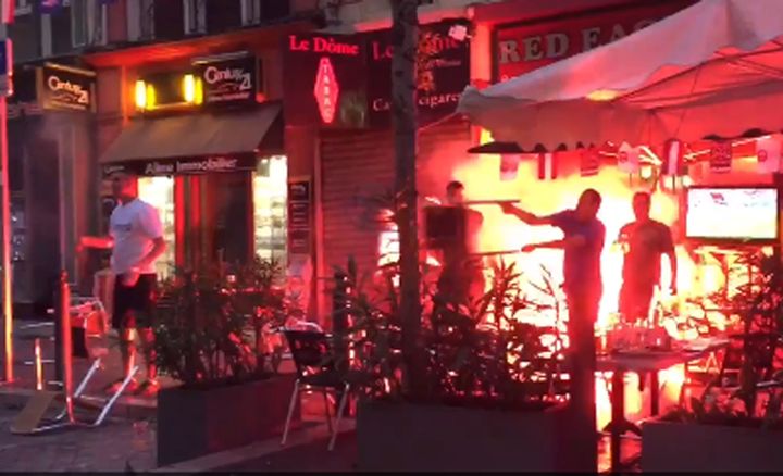 A flare burns and a man throws a chair at the Red Eagle Cafe in the Rue de la Republique, Marseille