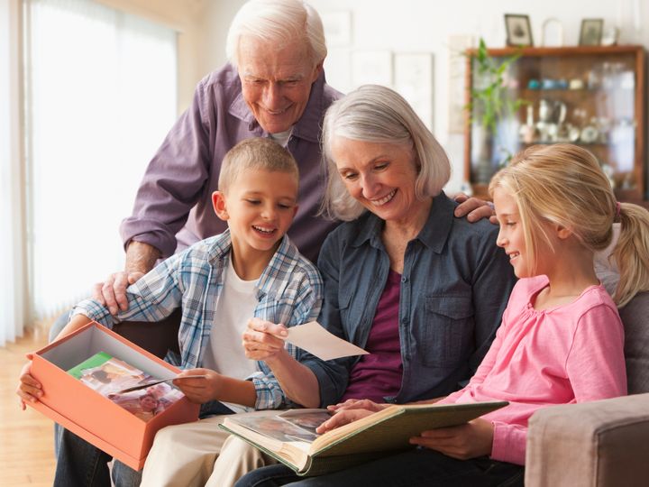 Caucasian couple looking at photographs with grandchildren KidStock via Getty Images