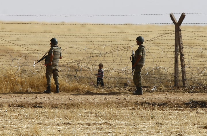 Turkish soldiers stand guard as a Syrian refugee boy waits behind the border fences to cross into Turkey on the Turkish-Syria