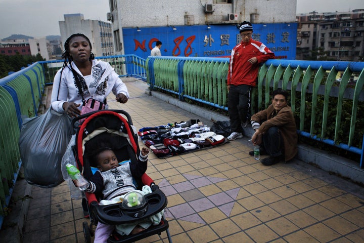 FILE PHOTO: An African woman with a baby in a stroller passes a pedestrian bridge where Chinese street vendors are trying to