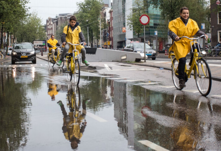 Hardy Amsterdam cyclists navigate puddles in Nieuwezijdskolk, central Amsterdam.