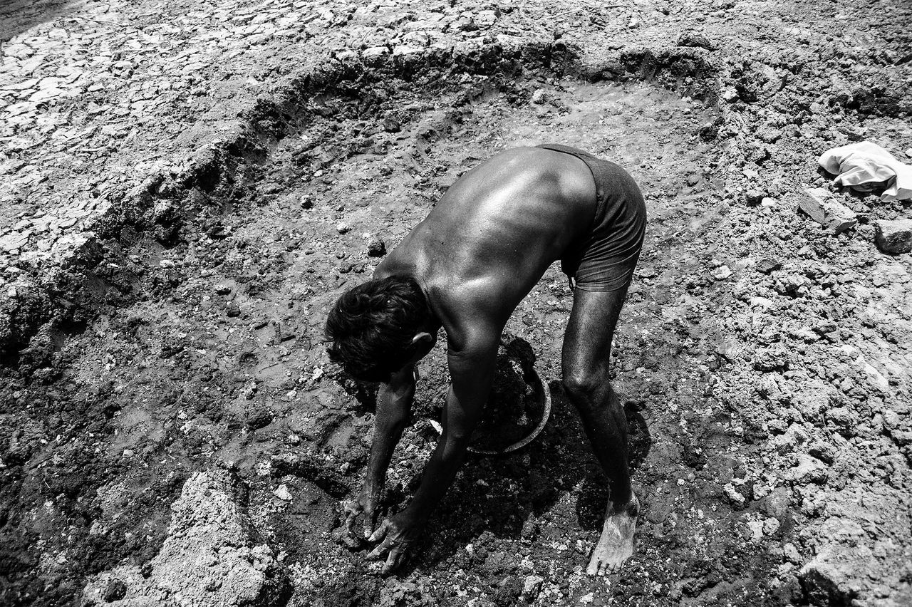 Dayaram digs out dirt from the bottom of a dry pond near Dhikwaha.