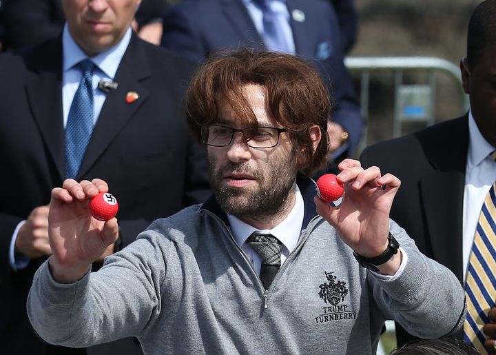 Comedian Simon Brodkin, also known as Lee Harris, hands out golf balls emblazoned with swastikas during the Trump event