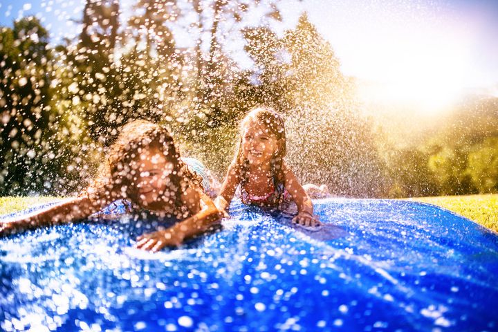 Happy little girls laughing while sliding down a slippery water slide in the sun wundervisuals via Getty Images