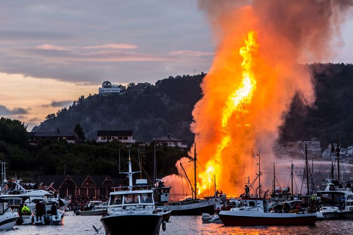 A giant bonfire burns by the water.