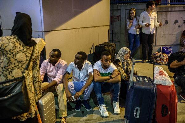 i         /People wait with their luggage outside the airport.