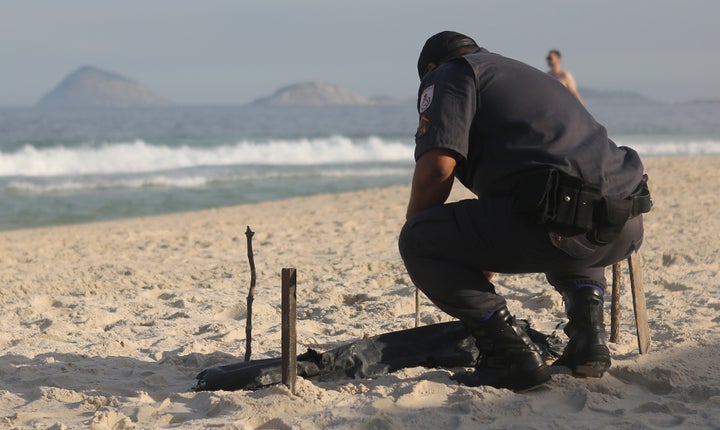 A police officer kneels over a body part, covered in a plastic bag, which was discovered on Copacabana Beach near the Olympic beach volleyball venue on Wednesday in Rio de Janeiro, Brazil.