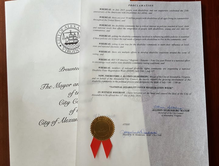 Image Description: two sheets of paper overlapping. The top sheet is translucent and contains the language of the proclamation issued by the City of Alexandria, Virginia in recognition of National Disability Voter Registration Week. The gold and red seal of the city is at the bottom of the page along with the signature of the Mayor and witness. The bottom sheet has the seal of the city in black and white, and the words "Presented by the Mayor and Members of the City Council of the City of Alexandria, Virginia" in cursive are partially visible.