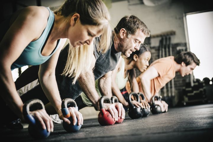 gym personal trainer doing push ups on kettle bells with small group of people in Gym. ferrantraite via Getty Images