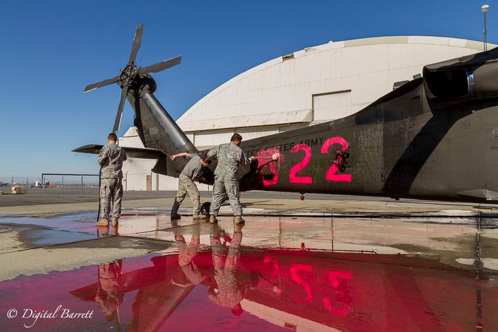 Sergeant Denis Pokidov, Private First Class Joseph Cafferkey, and Specialist Michael Luong work to remove the distinctive markings used to make the helicopters more visible when the Cal Guard helicopters are used for fire fighting.