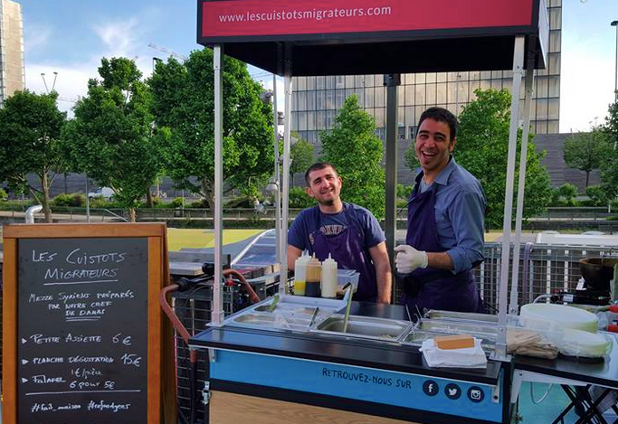 Two Syrian cooks, working for Les Cuistots Migrateurs, serving Syrian appetizers at a Paris venue. 