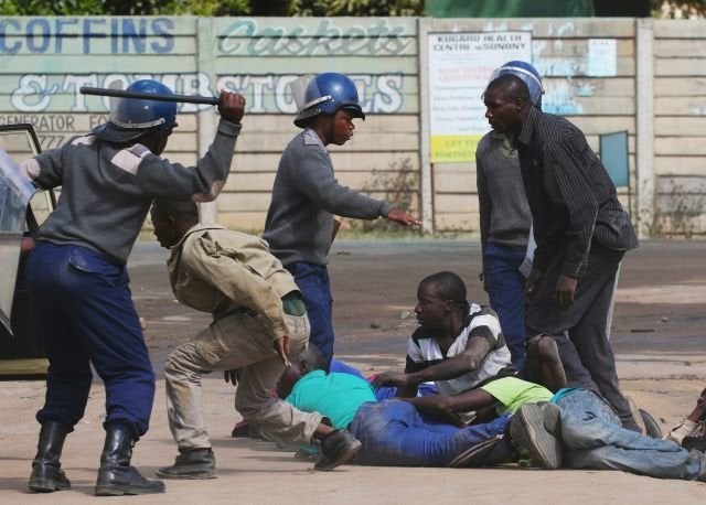 Riot police detain people after a protest by taxi drivers turned violent in Harare on July 4, 2016.