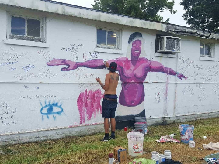 An artist paints a mural depicting Alton Sterling.