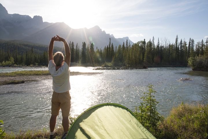 Camper stretches beside mountain river, sunrise Ascent Xmedia via Getty Images