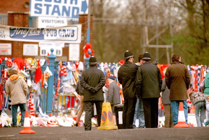 Policemen stand outside the Leppings Lane end of the Hillsborough ground, as the flowers pile up in memory of the fans that died