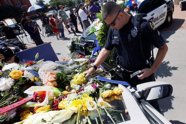 A Dallas police officer observes a moment of silence after putting some flowers on a police car that makes up part of a makes
