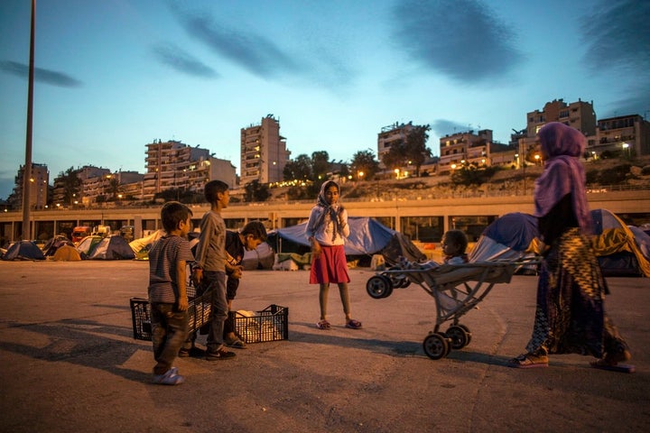 A refugee family stand at dusk against a battery of concrete apartment blocks in the Athenian port of Piraeus.