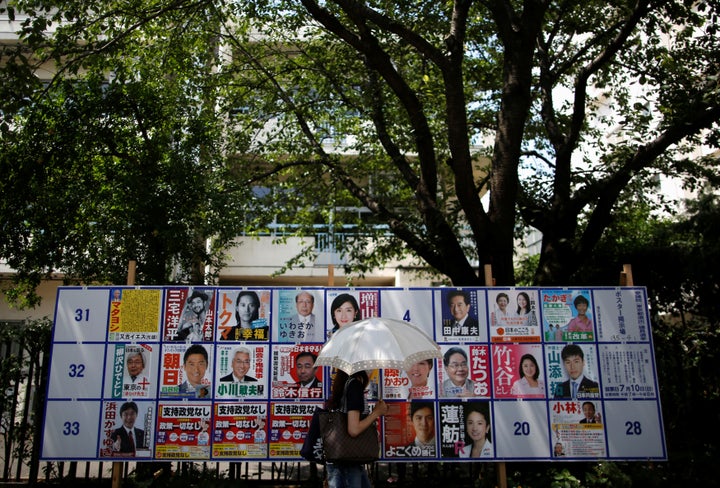 A voter walks past in front of election campaign posters for Japan's upper house election, on a street in front of a polling