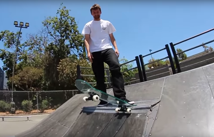 A skateboarder is seen preparing to drop down on a ramp with a glass deck.