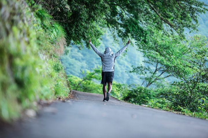 Portrait of young black man exercising in Kyoto, Japan. He is having fun and raising hand up in the air. Green forest in the back. AzmanL via Getty Images