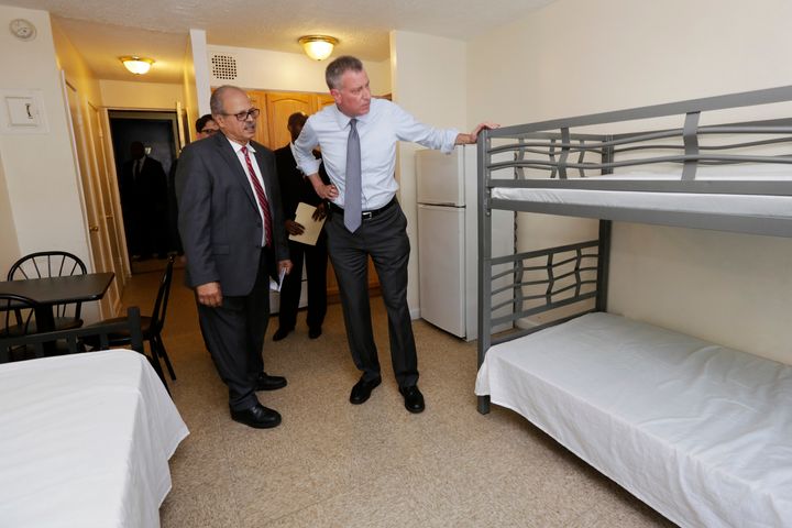 NEW YORK, NY - MAY 11: New York Mayor Bill de Blasio, right, listens to Acacia Network CEO Raul Russ, foreground left, as he visits a room at the Corona Family Residence, a homeless facility, May 11, 2015 in the Queens borough of New York City. Mayor deBlasio made an announcement on his effort to combat the city's homelessness crisis. Also in the visit are Dept. of Investigations Commissioner Mark Peters, background left, and Dept. of Homeless Services Commissioner Gilbert Taylor. (Photo by Richard Drew-Pool/Getty Images)